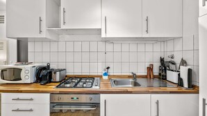 A modern kitchen with white cabinets, a microwave, a toaster, a gas stove, a sink, and wooden countertops. - primeflats - Apartment Leberstr 58 Nr. 3 (Berlin)