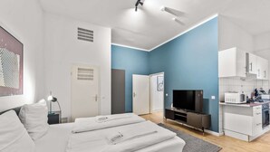 A modern hotel room with a bed, a TV, a kitchenette, and a bathroom. - primeflats - Apartment Leberstr 58 Nr. 3 (Berlin)