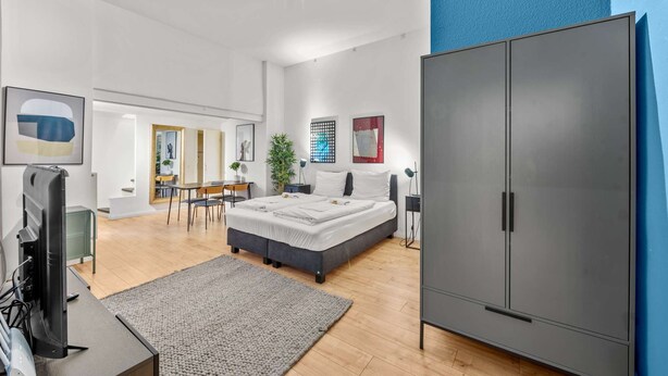 A modern bedroom with a large wardrobe, a bed, a desk, and a dining area. - primeflats - Apartment Leberstr 58 Nr. 3 (Berlin)
