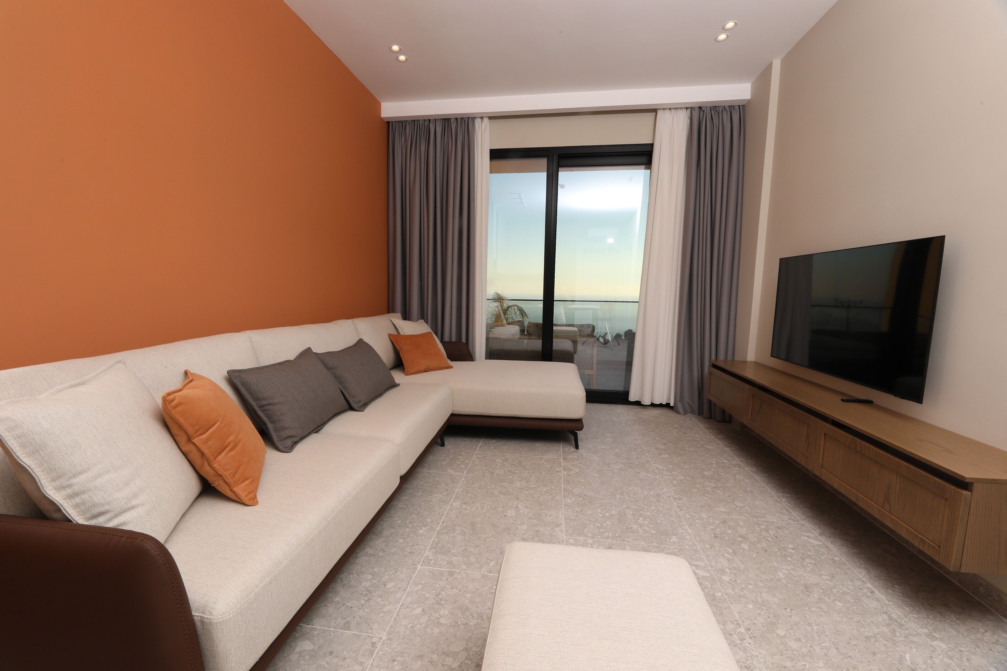 A modern living room with a sofa, ottoman, and a TV on a wooden stand.