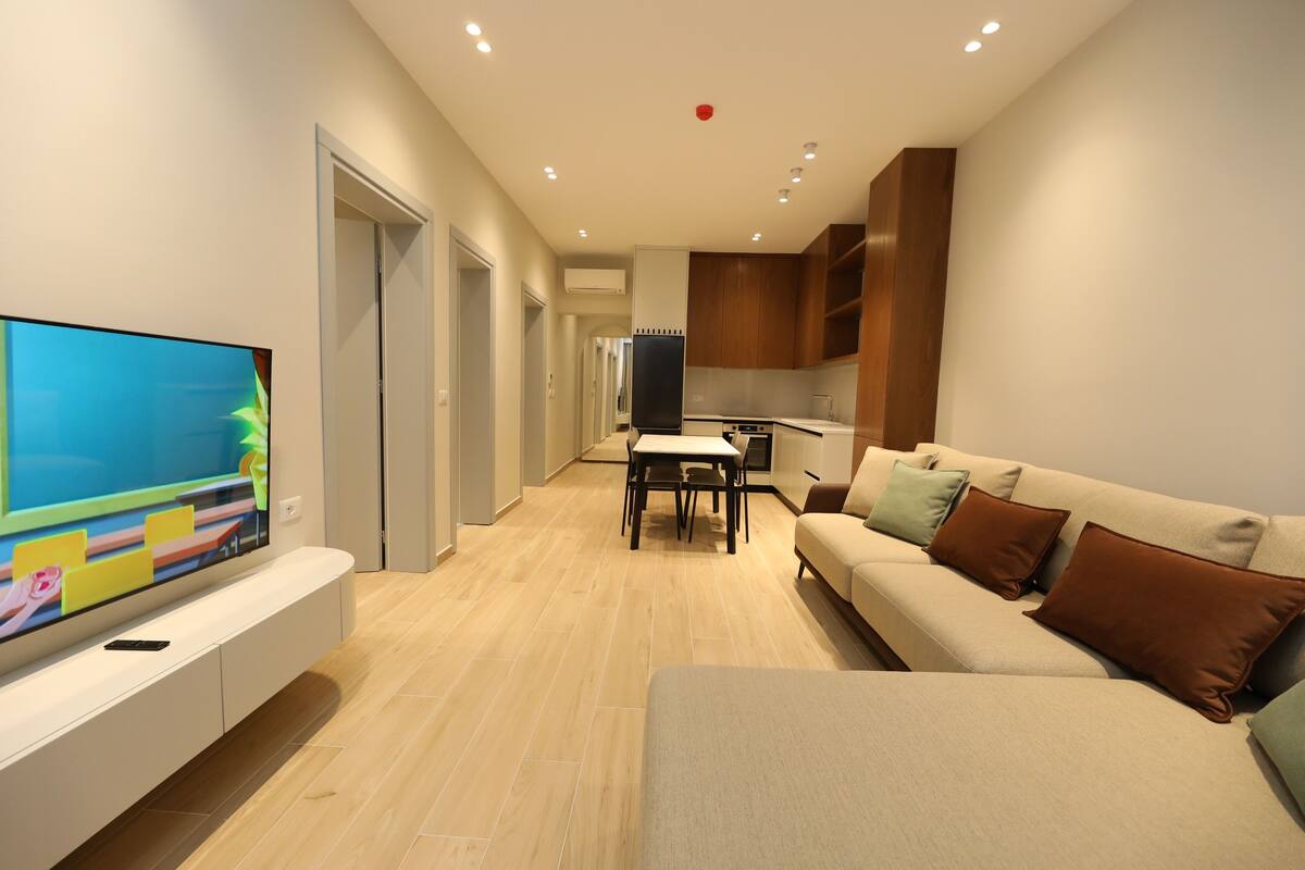 A modern living room with a flat-screen TV, a sofa, and a dining area with a table and chairs.