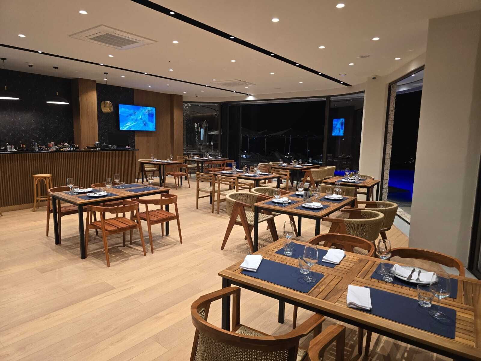 A restaurant with multiple tables and chairs, a bar area, and a television screen.