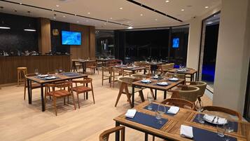 A restaurant with multiple tables and chairs, a bar area, and a television screen.