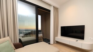 A modern hotel room with a large bed, a flat-screen TV mounted on the wall, and a balcony with a city view. - Aurum Hotel (Himarë)