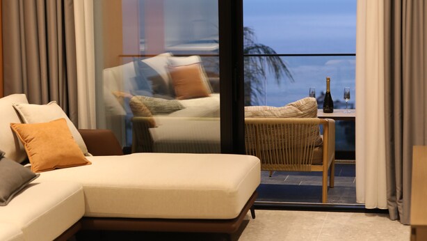 A modern living room with a sofa, a wicker chair, and a table with a bottle and glass. - Aurum Hotel (Himarë)