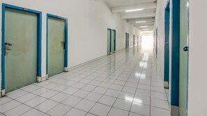 A long, narrow hallway with white tiled floors and doors with blue trim. - Hotel Margadana (Tegal)