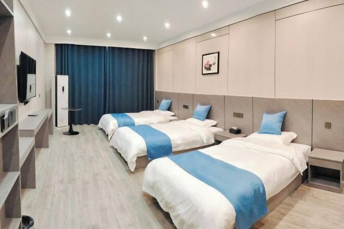A hotel room with three beds, a desk, and a TV.