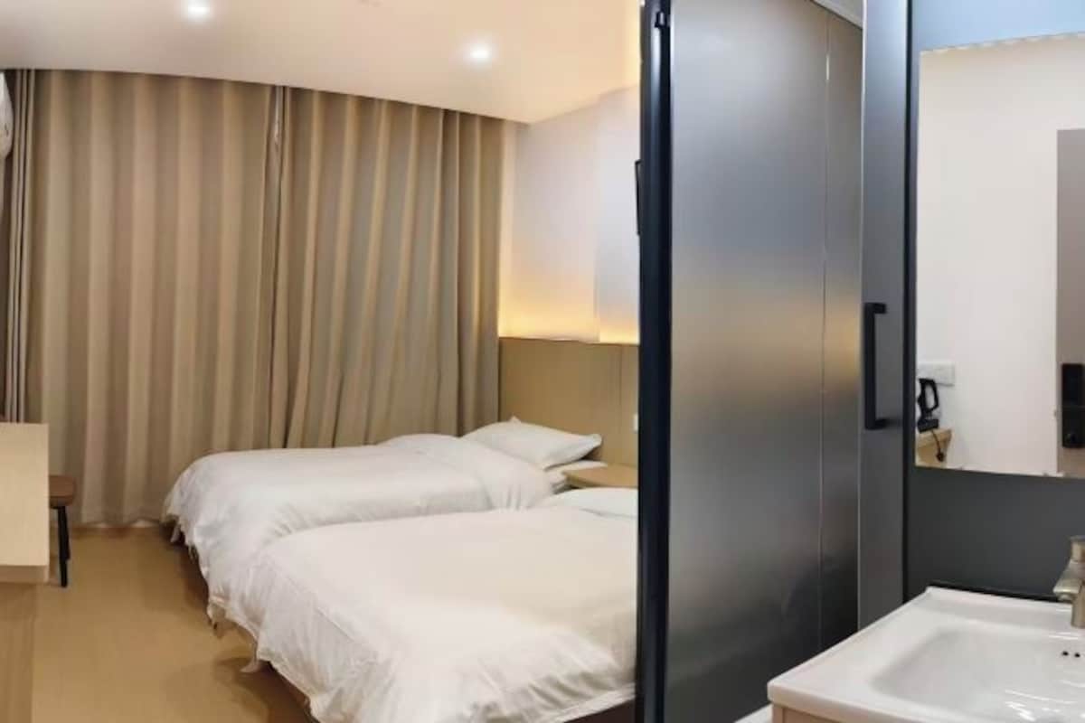 Ett hotellrum med två sängar, ett badrum med handfat och ett stort fönster med gardiner.