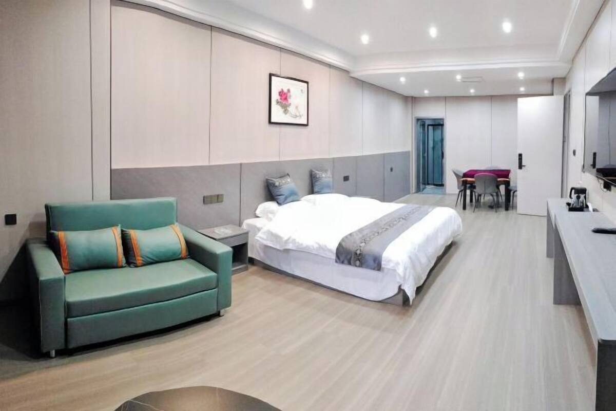 A modern hotel room with a bed, a green sofa, a desk, and a chair.