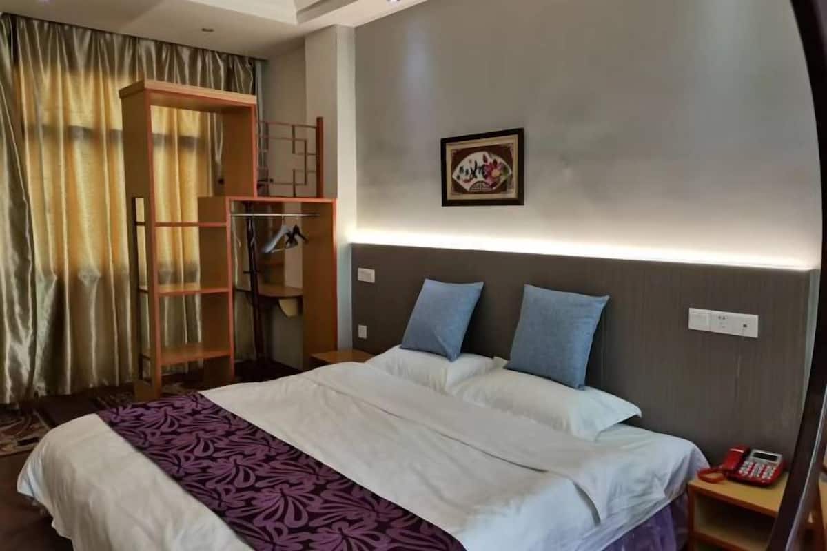 A hotel room with a bed, a wardrobe, a bedside table with a phone, and a wall-mounted light.