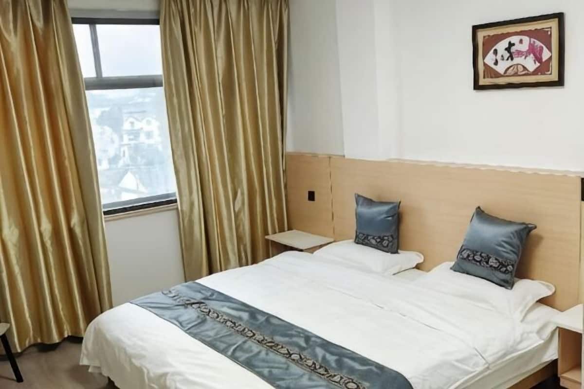 Quarto de hotel com cama, duas almofadas, mesa de cabeceira, janela com cortinas e um quadro na parede.