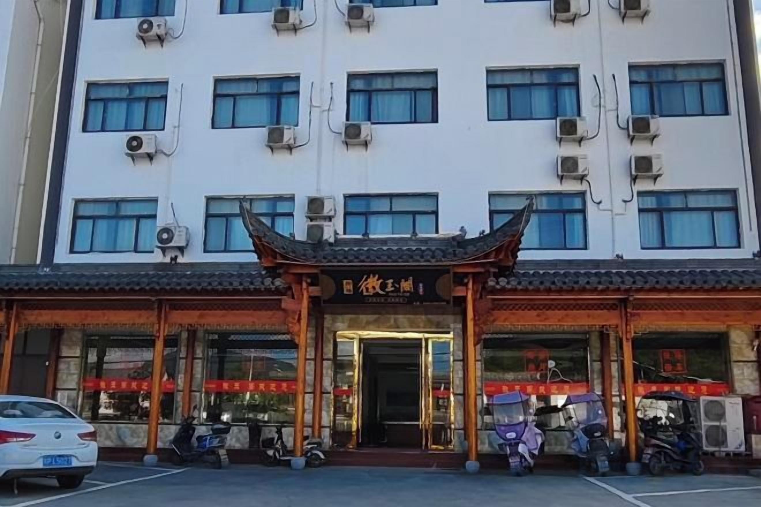 A building with a traditional Chinese architectural entrance, multiple windows, and a parking area with vehicles.