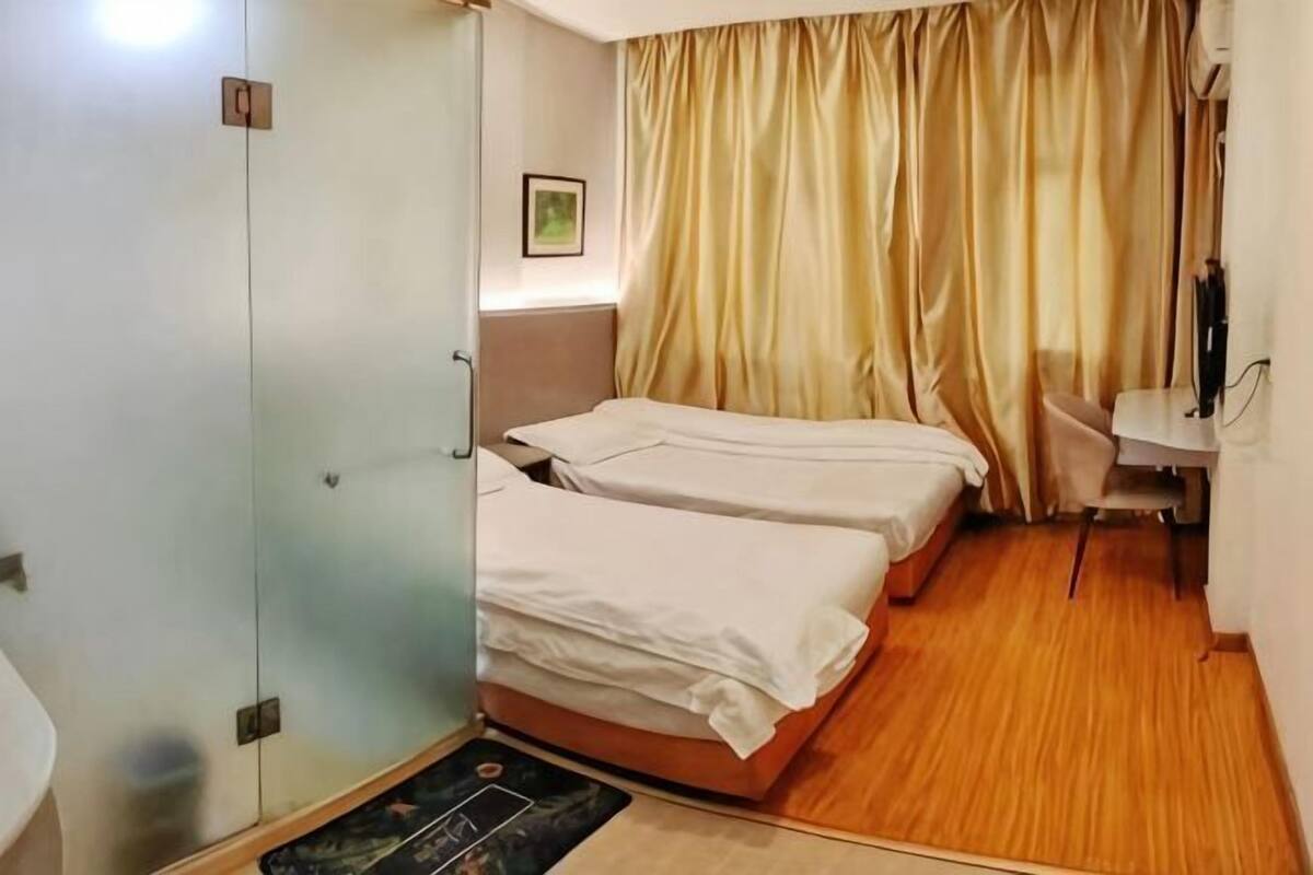 A hotel room with two beds, a small table, a chair, a wardrobe, and a curtain.
