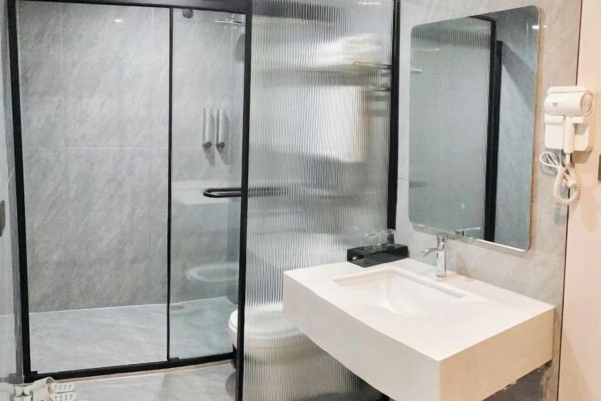Un baño moderno con ducha de vidrio, lavamanos blanco y espejo.