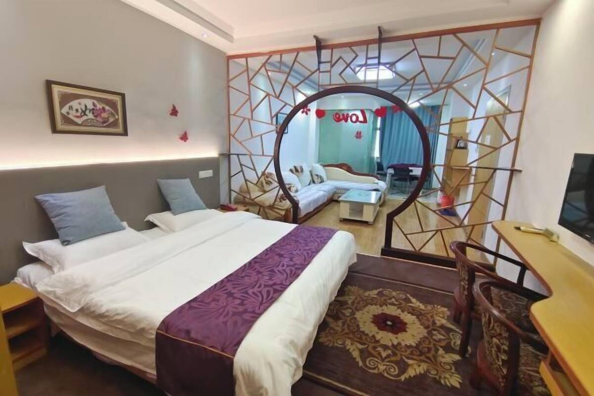 A hotel room with a bed, a desk, a chair, a TV, and a decorative mirror.
