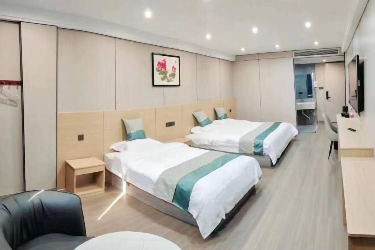 A hotel room with two beds, a desk, a chair, and a bathroom visible through an open door.