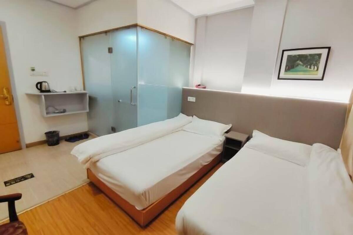A hotel room with two beds, a wardrobe, a shelf with toiletries, and a framed picture on the wall.