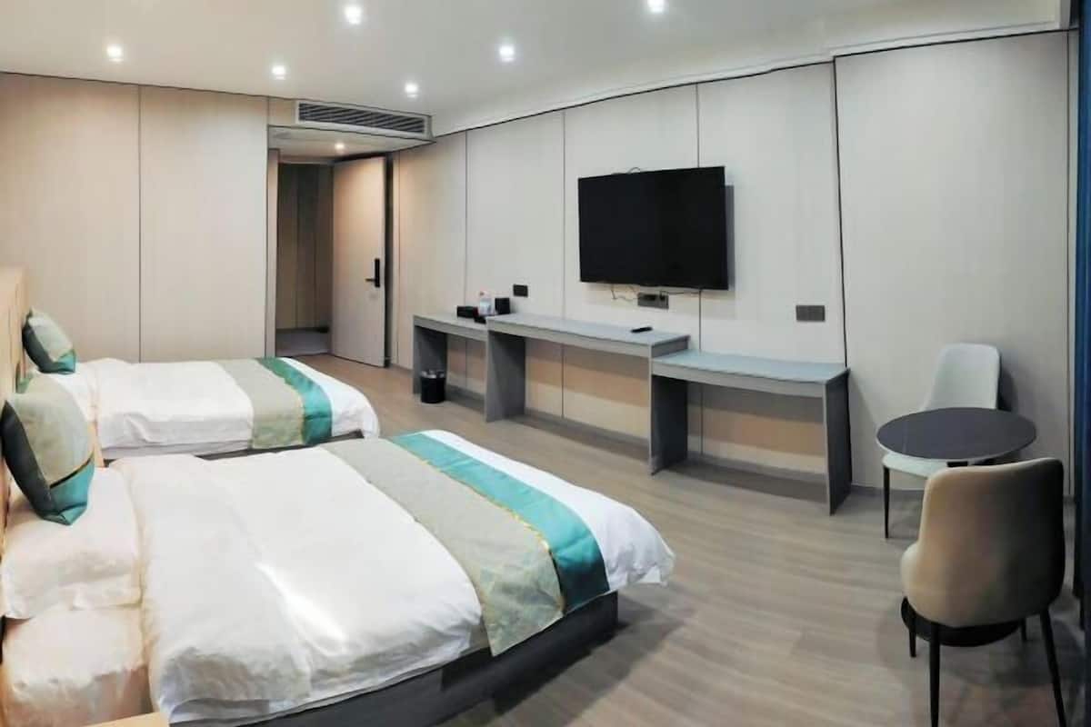 A hotel room with two beds, a TV, a desk, and a chair.