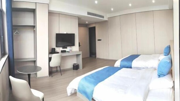 Habitación de hotel con dos camas, un escritorio, una silla, un televisor y un armario.