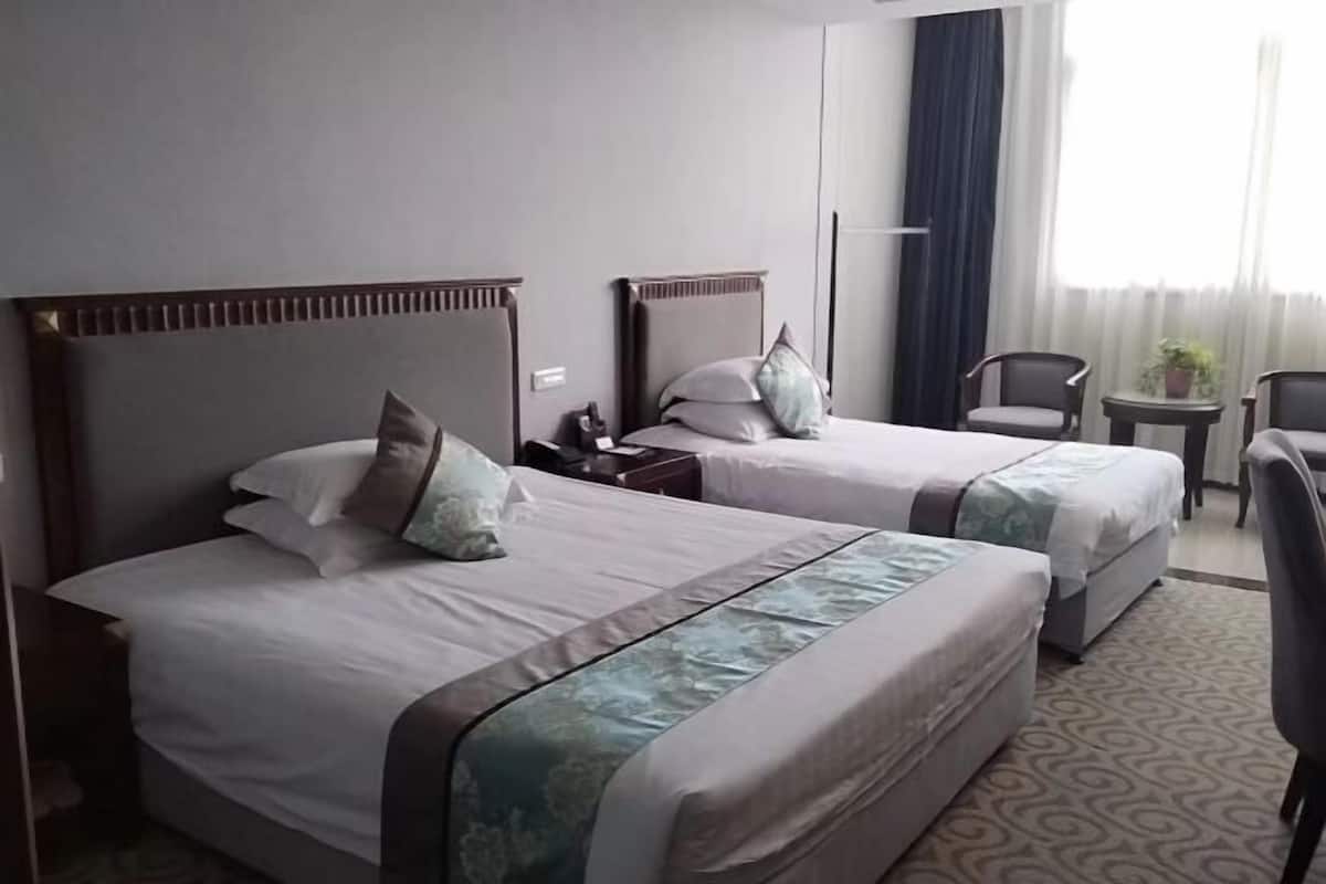 Habitación de hotel con dos camas, una mesita, una silla y una ventana con cortinas.