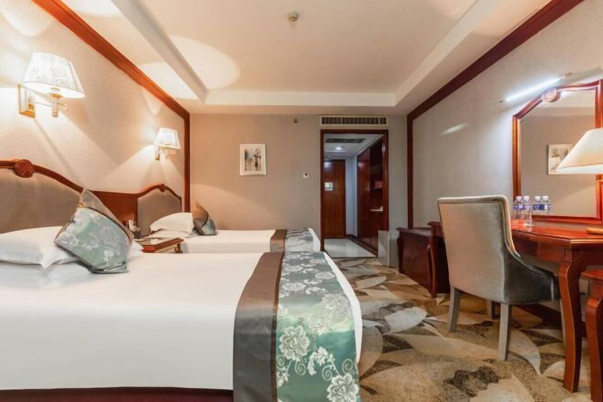 Habitación de hotel con dos camas, un escritorio, una silla, un espejo y una alfombra estampada.
