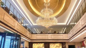 Eine geräumige Lobby mit einem prächtigen Kronleuchter, Marmorwänden und einer Glastrennwand, die in die untere Ebene führt.