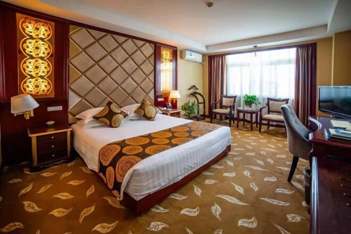 Habitación de hotel con una cama grande, un escritorio con televisor, una silla y una ventana con cortinas.