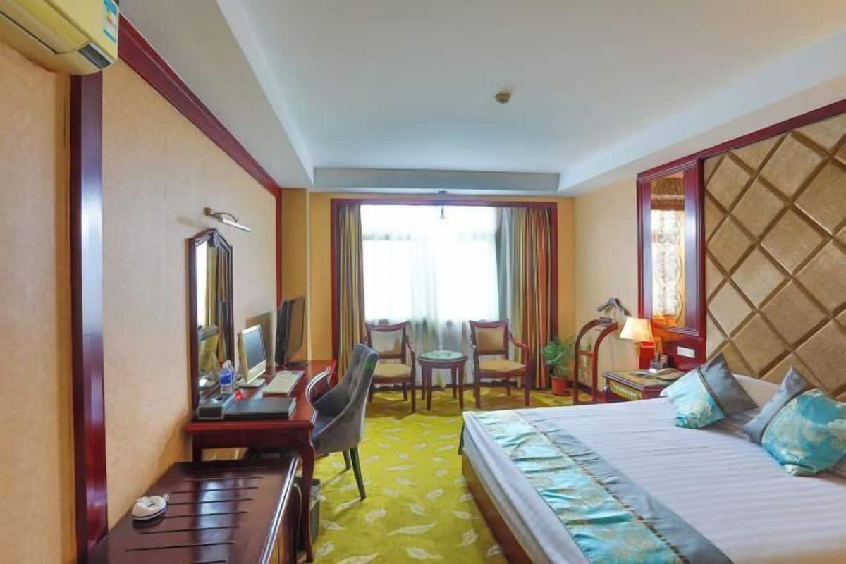 Una habitación de hotel con cama, escritorio, sillas, lámpara de escritorio y ventana con cortinas.
