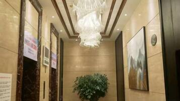 A hallway with marble walls, a chandelier, a potted plant, and framed artwork.