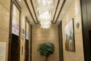 A hallway with marble walls, a chandelier, a potted plant, and framed artwork. - Shuyi International Hotel (Shucheng)