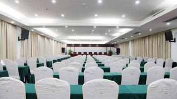 A conference room with rows of tables and chairs, a stage with a podium, and a large screen.