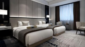 Ein modernes Hotelzimmer mit zwei Betten, einem großen Fenster mit Vorhängen, einem Nachttisch und einem Sessel.