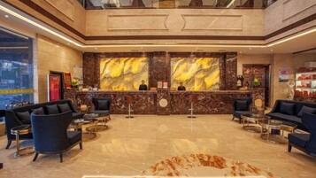 A hotel lobby with a reception desk, seating area, and a large marble wall.