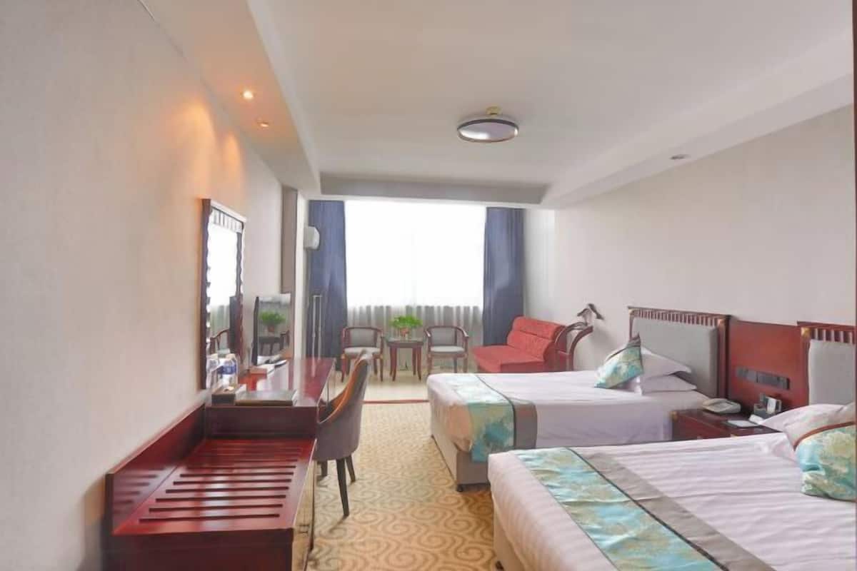Habitación de hotel con dos camas, un escritorio, una silla, una mesita y una ventana con cortinas.