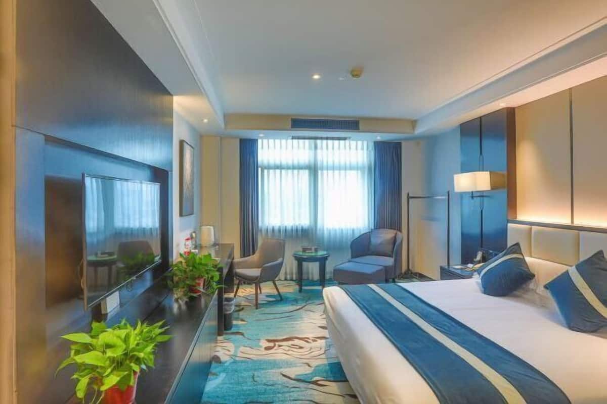 Una habitación de hotel moderna con una cama grande, un televisor de pantalla plana, un escritorio con una silla y una mesita.