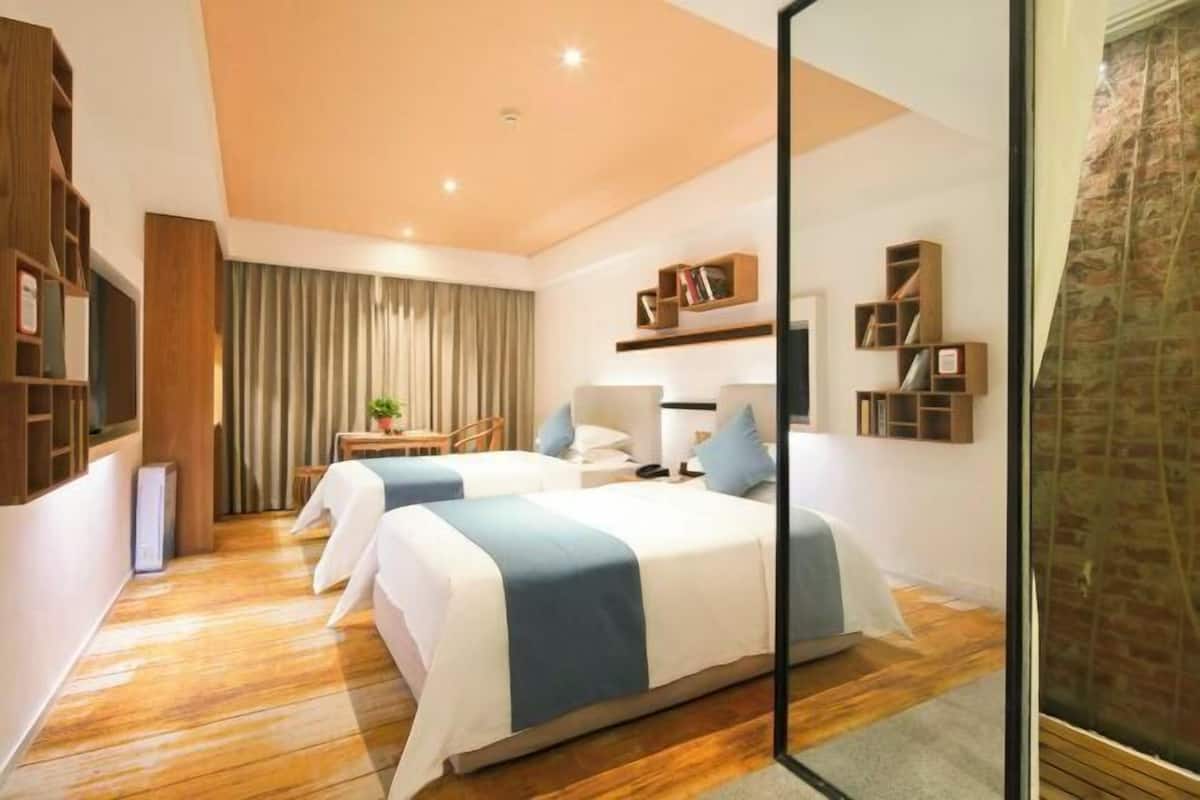 A modern hotel room with two beds, a desk, a chair, and a small table with a plant.