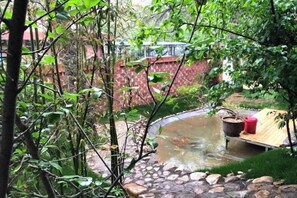 A garden with a small pond, a wooden bench, and a red wall in the background. - Wending Yaxuan Hotel (Zhengzhou)