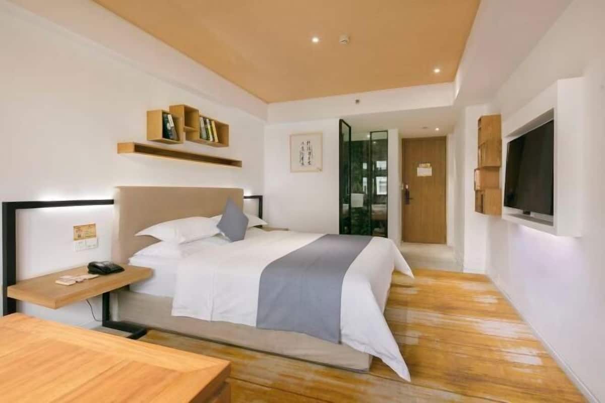 A modern hotel room with a bed, bedside table, and a TV mounted on the wall.