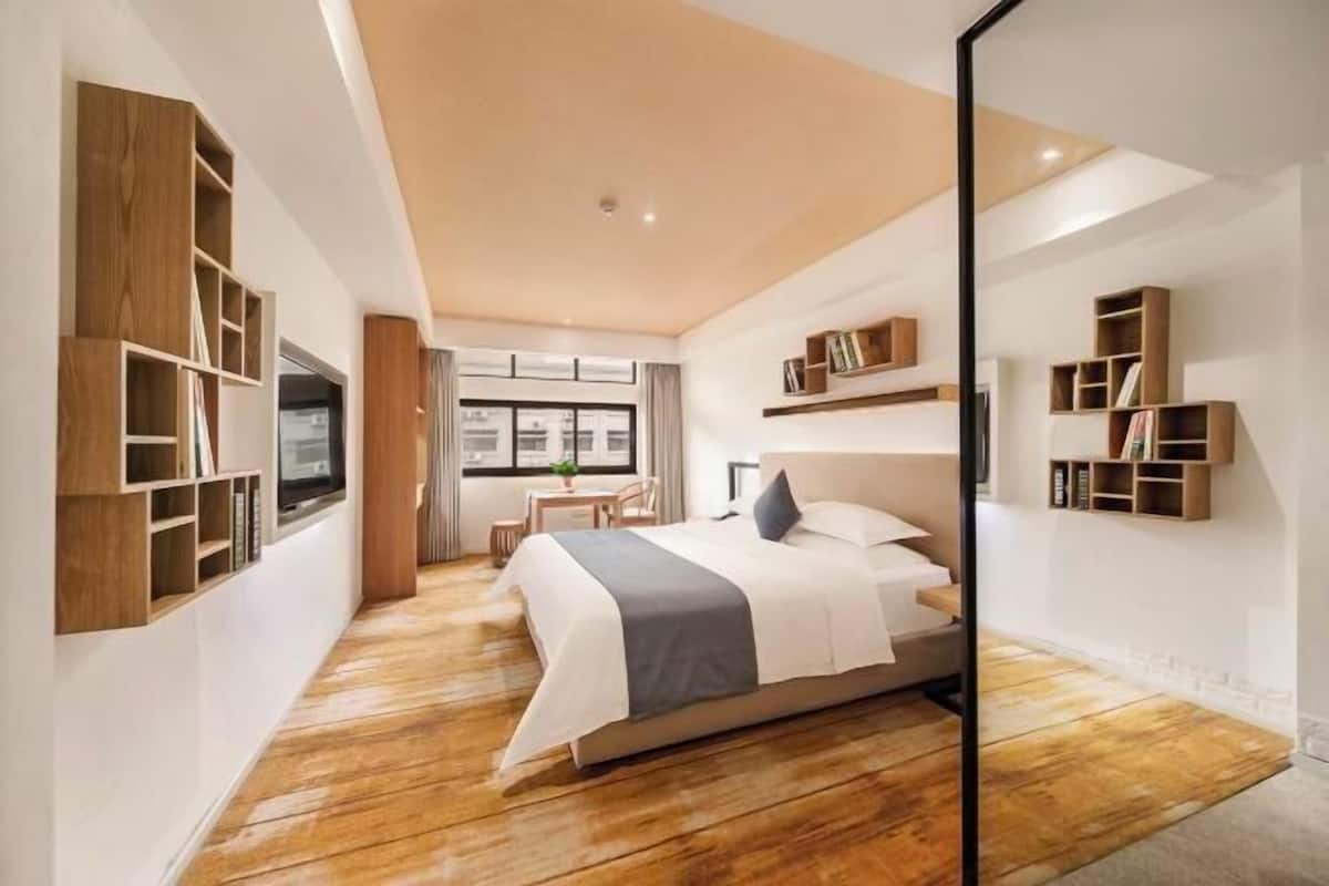 A modern bedroom with a large bed, built-in wooden shelving, and a view of the outdoors.