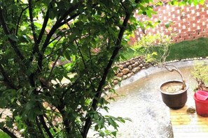 Un jardín con fuente de agua, pared de ladrillo y terraza de madera.
