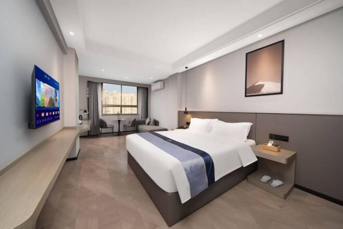 Una habitación de hotel moderna con una cama grande, un televisor montado en la pared, un escritorio con una silla y una ventana con vistas a la ciudad.