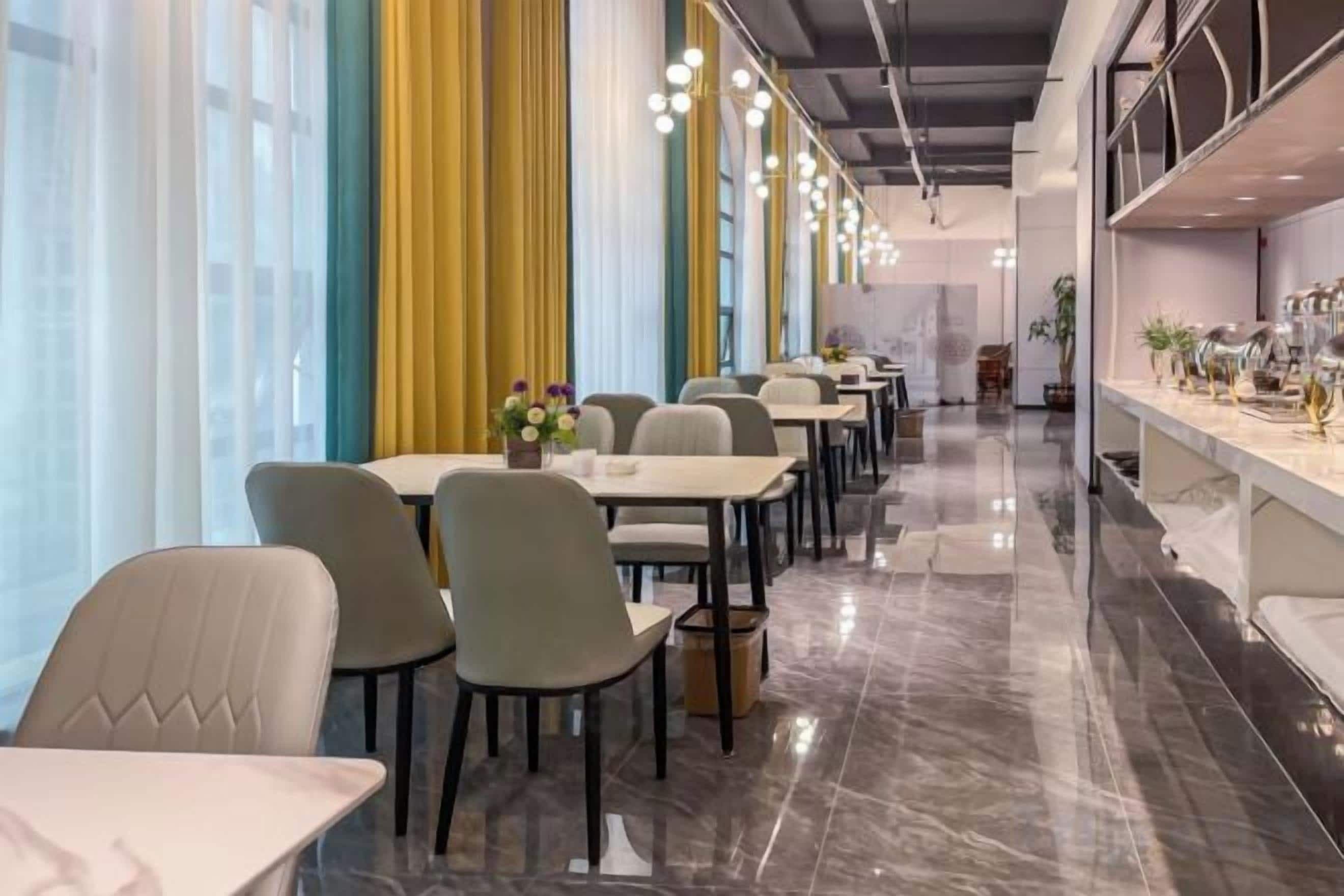 A modern dining area with long tables and chairs, a marble floor, and a view of the kitchen area.