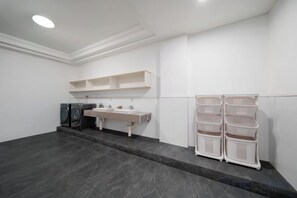 Une salle de bain avec un carrelage foncé, un lavabo blanc et un coin buanderie avec des paniers.