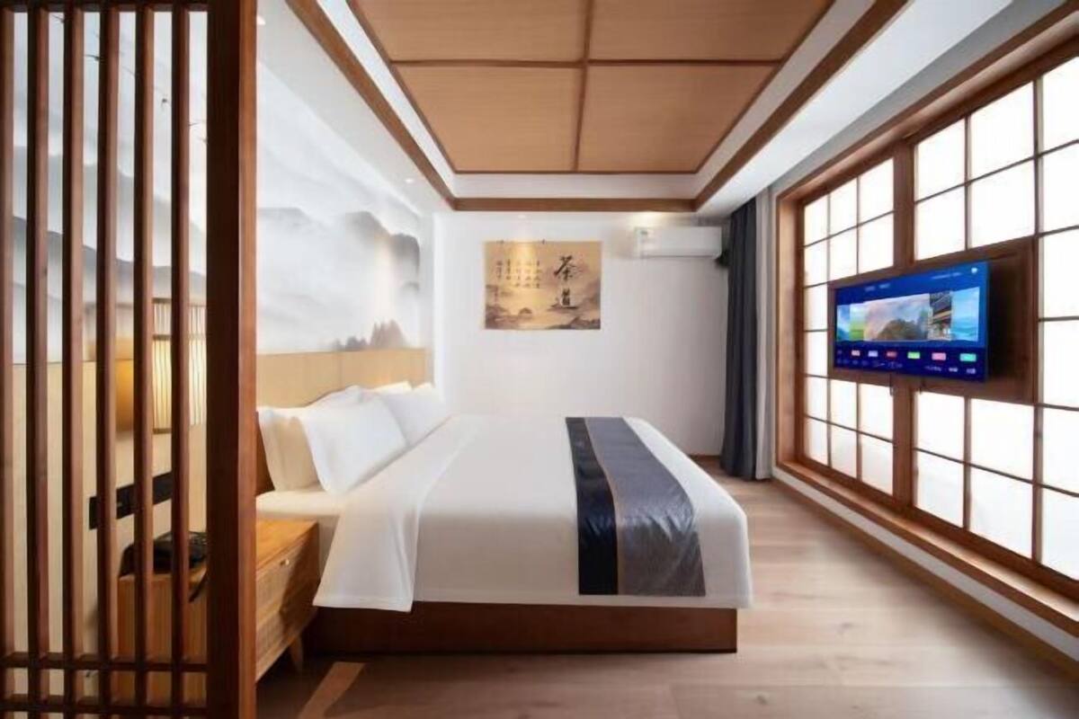 Habitación de hotel con cama, televisor y ventana grande con vistas a montañas.