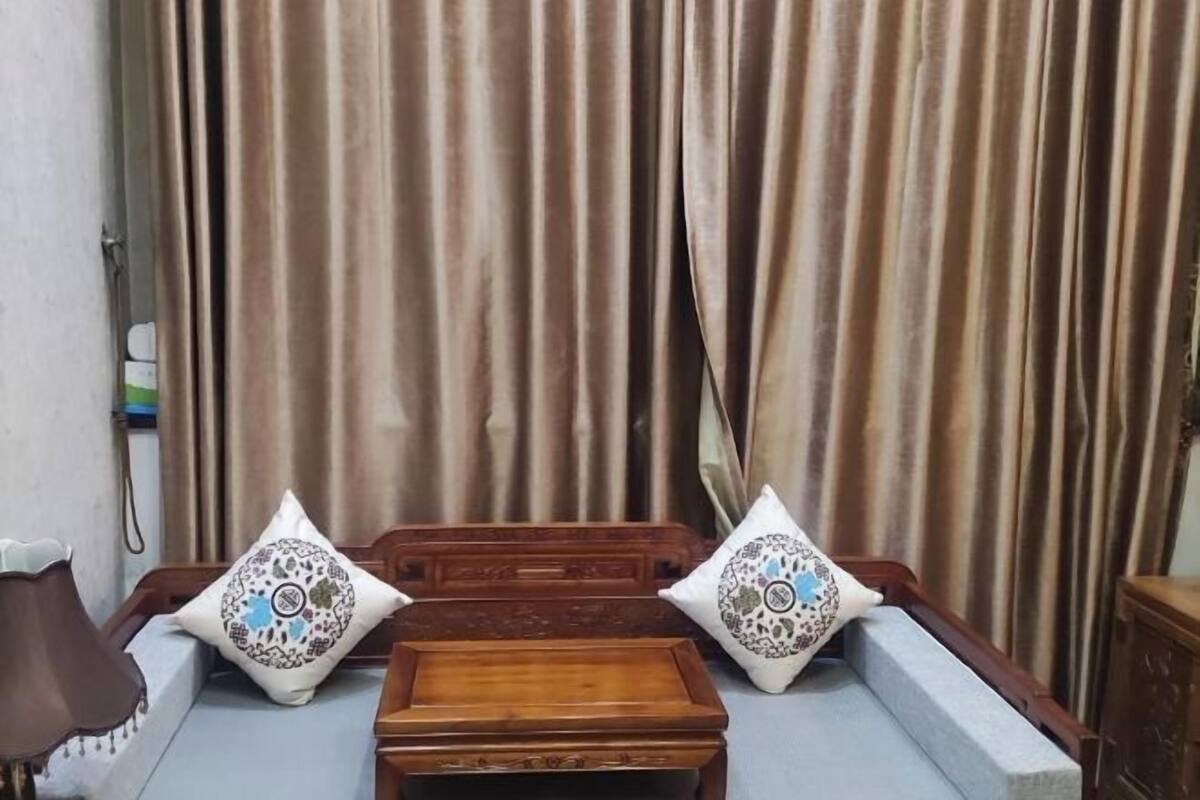 Una stanza con un letto, due cuscini decorativi, un tavolino di legno e tende.