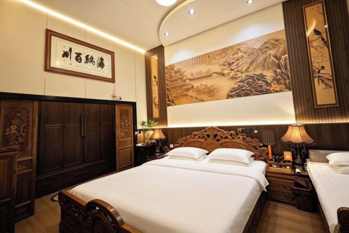 A hotel room with a large bed, wooden headboard, and traditional artwork on the wall.
