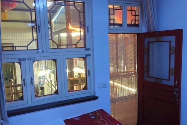 A room with a window overlooking a street, a door with decorative elements, and a red cushion on the floor. - Pingyao Xingfu House (Pingyao County)