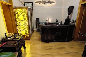 A room with a wooden floor, a desk with a lamp, and a decorative wall panel.