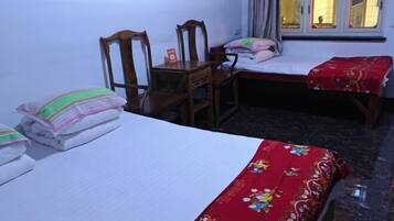 A bedroom with two beds, a wooden chair, a small table, and a window with curtains.