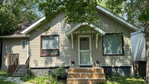 A single-story house with a front porch, a small front yard, and a wooden staircase leading to the front door.